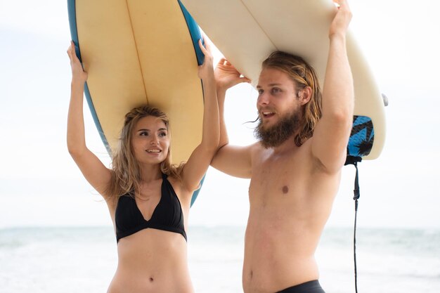 Junge Mann und Frau halten Surfbretter auf den Köpfen und gehen ins Meer, um zu surfen