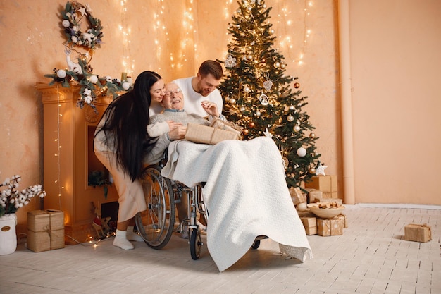 Junge Mannfrau und ihr alter Vater auf einem Rollstuhl, der nahe Weihnachtsbaum sitzt