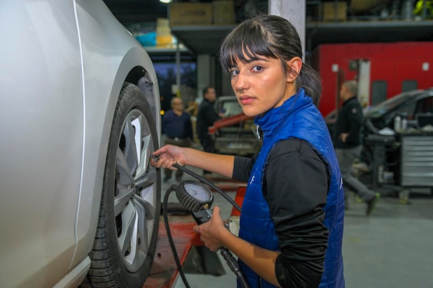 Junge Mechanikerin überprüft den Luftdruck der Reifen eines Autos