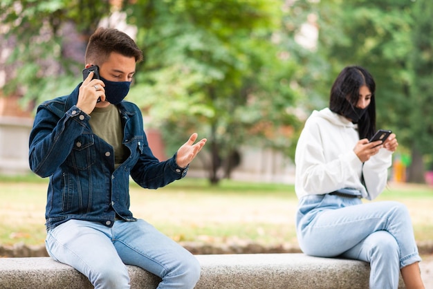 Junge Menschen, die ihr Smartphone benutzen, während sie eine Maske im Freien tragen, Coronavirus und soziale Distanzierung