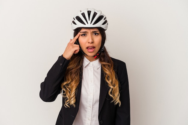 Junge mexikanische Frau, die mit dem Fahrrad zur Arbeit fährt, isoliert auf weißem Hintergrund, der eine Enttäuschungsgeste mit dem Zeigefinger zeigt.