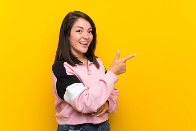 Junge mexikanische Frau über lokalisiertem gelbem Zeigefinger auf die Seite