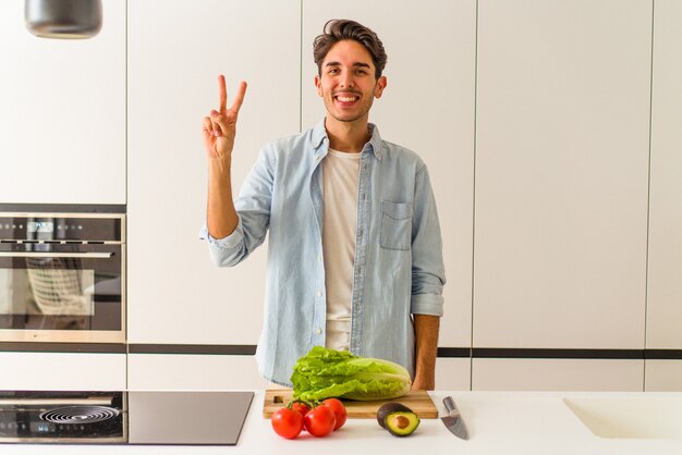 Junge Mischlinge, die einen Salat zum Mittagessen vorbereiten, der Nummer zwei mit den Fingern zeigt.