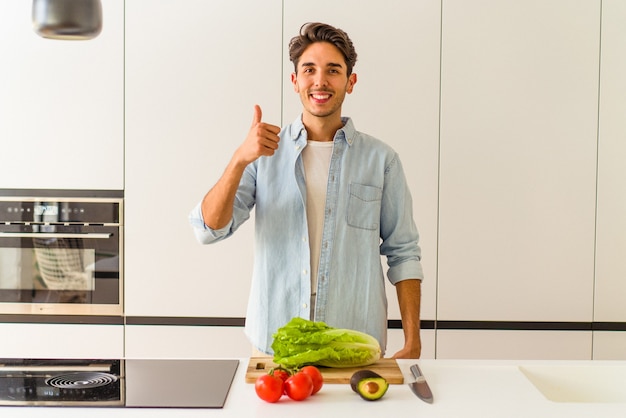 Junge Mischlinge, die einen Salat zum Mittagessen zubereiten, lächeln und Daumen hochheben