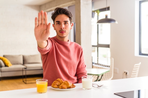 Junge Mischlinge, die morgens in einer Küche frühstücken, stehen mit ausgestreckter Hand und zeigen Stoppschild, um Sie zu verhindern.