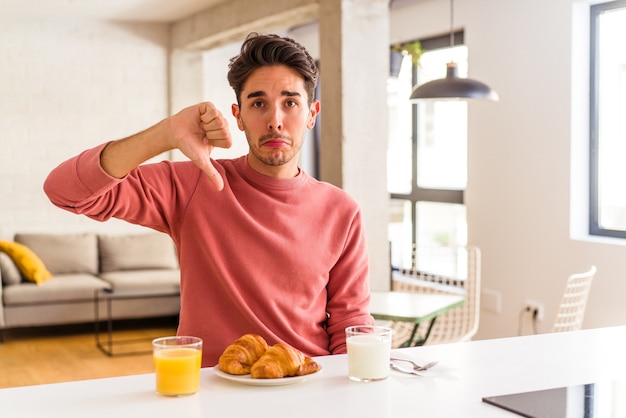 Junge Mischlinge, die morgens in einer Küche frühstücken und eine Abneigungsgeste zeigen, Daumen nach unten. Meinungsverschiedenheit Konzept.