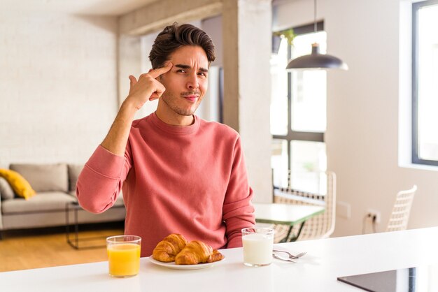 Junge Mischlinge, die morgens in einer Küche frühstücken und mit dem Finger auf den Tempel zeigen, denken, sich auf eine Aufgabe konzentrieren.