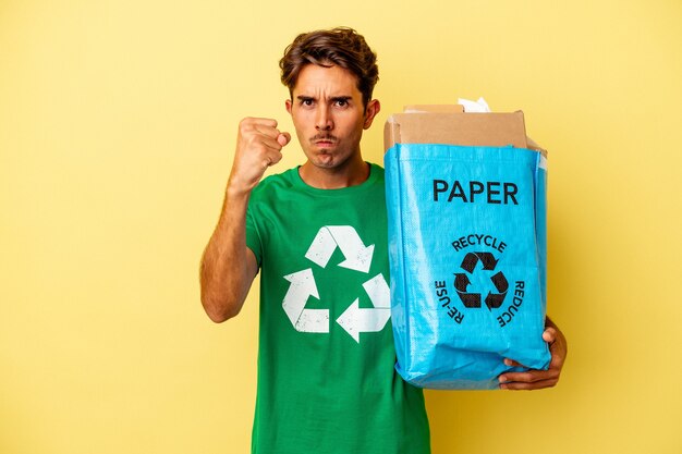 Junge Mischlinge Mann Recyclingpapier isoliert auf gelbem Hintergrund mit Faust zur Kamera, aggressiven Gesichtsausdruck.