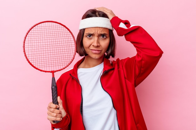 Junge Mischlingsfrau, die Badminton spielt, isoliert auf rosa Wand geschockt, sie hat sich an wichtiges Treffen erinnert.