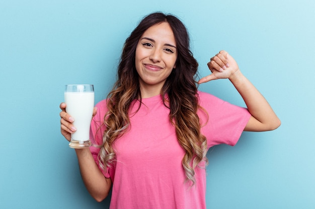 Junge Mischlingsfrau, die ein Glas Milch einzeln auf blauem Hintergrund hält, fühlt sich stolz und selbstbewusst, Beispiel zu folgen.