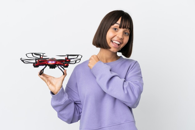 Junge Mischlingsfrau, die eine Drohne hält, die auf weißem Hintergrund lokalisiert wird und einen Sieg feiert