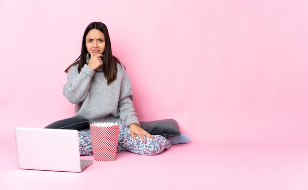 Junge Mischlingsfrau, die Popcorn isst, während sie einen Film auf dem Laptop sieht, der Zweifel hat