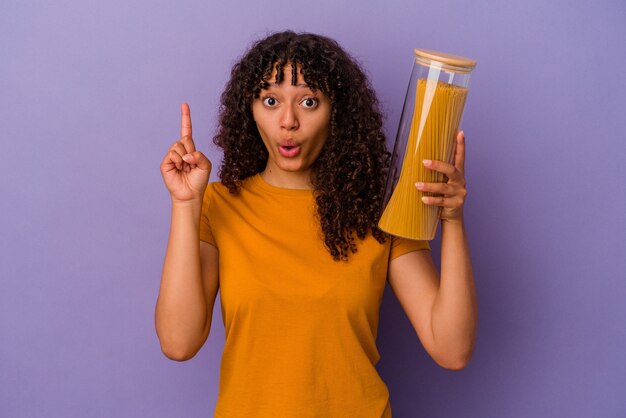 Junge Mischlingsfrau, die Spaghetti einzeln auf violettem Hintergrund hält und eine großartige Idee hat, Konzept der Kreativität.