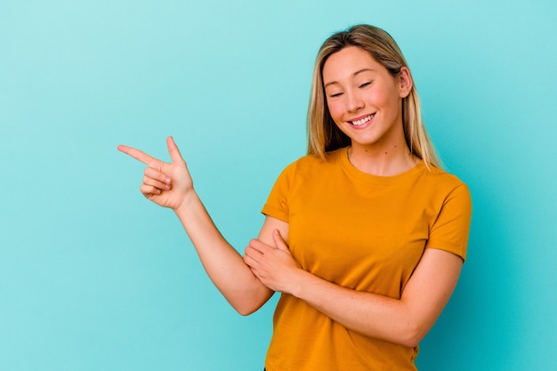 Junge Mischlingsfrau lokalisiert auf der blauen Wand, die fröhlich mit Zeigefinger weg zeigt.