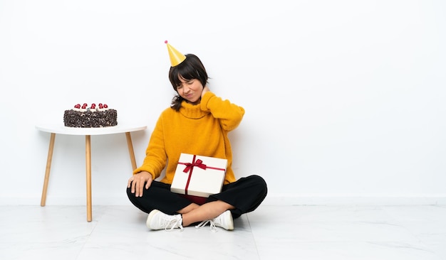 Junge Mischlingsfrau mit einem Geschenk auf dem Boden sitzend isoliert auf weißem Hintergrund mit Nackenschmerzen