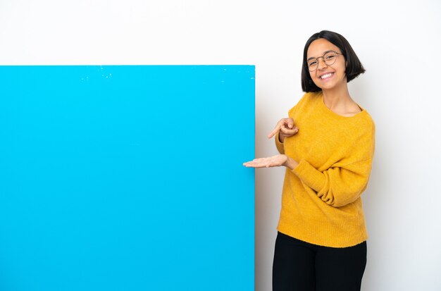 Junge Mischlingsfrau mit einem großen blauen Plakat lokalisiert auf weißem Hintergrund, der imaginären Copyspace auf der Handfläche hält, um eine Anzeige einzufügen