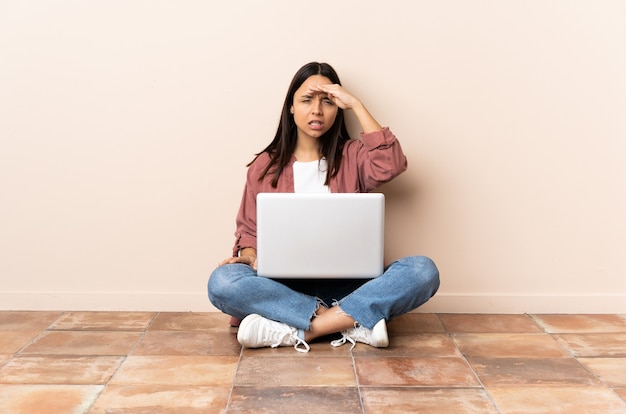 Junge Mischlingsfrau mit einem Laptop, der auf dem Boden sitzt