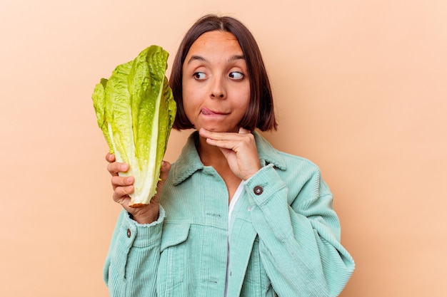 Foto junge mischrassenfrau, die einen salat lokalisiert auf beige wand hält