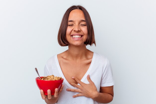 Junge Mischrassenfrau, die Müsli lokalisiert auf weißem Hintergrund lacht und Spaß hat isst.