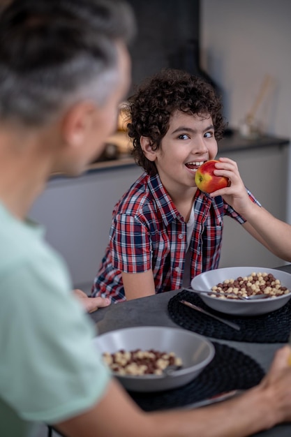 Junge mit Apfel in der Nähe des Mundes, der den Mann ansieht