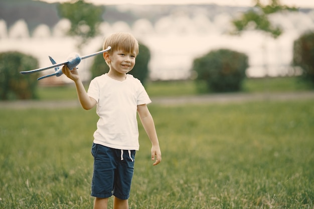 Junge mit blonden Haaren, die auf einem Gras mit einem Flugzeugspielzeug spielen. Junge mit weißem T-Shirt und blauen Shorts