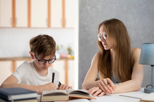 Junge mit Brille ist hart bei der Arbeit und schreibt seine Hausaufgaben. Ein junger Tutor hilft dem Schüler beim Unterricht. Häuslicher Unterricht.