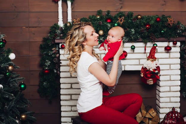 Junge mit der schönen blonden Mutter, die in verziertem Haus für Weihnachten umfasst