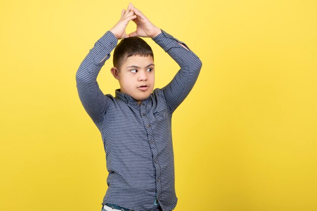 Junge mit Down-Syndrom posiert über gelber Wand.