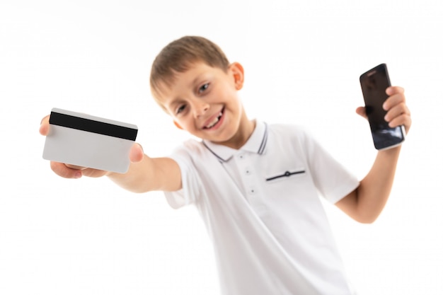 Junge mit einem Telefon in der Hand hält eine Kreditkarte mit einem Modell auf Weiß heraus