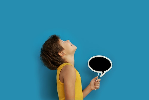 Junge mit einer leeren tafel für den text in der hand auf einer blauen wand