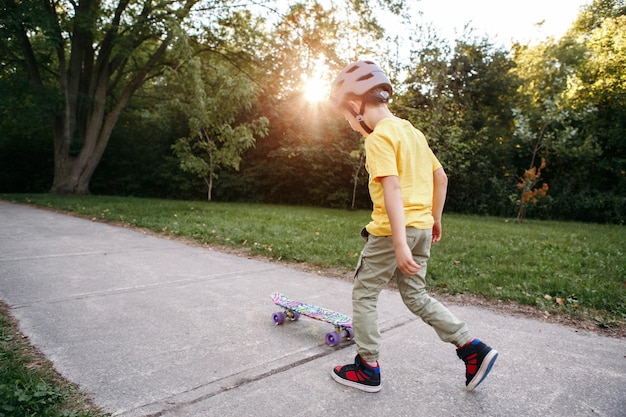 Foto junge mit grauem helm fährt skateboard im park an einem sommertag, saisonale outdoor-aktivität für kinder