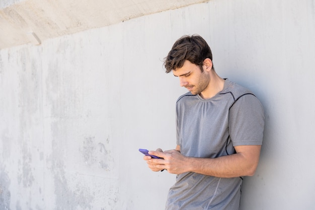 Junge mit Handy an die Wand gelehnt in Grau gekleidet