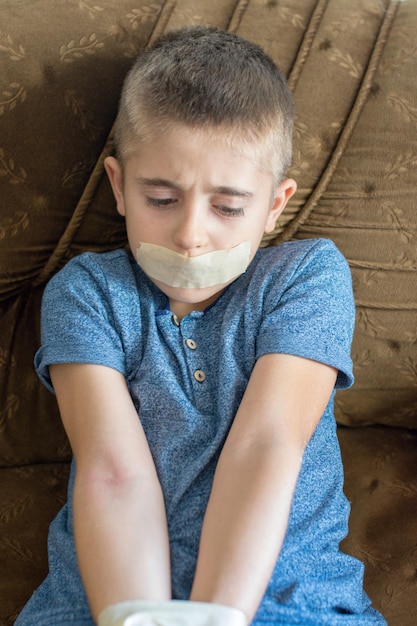 Foto junge mit klebeband am mund sitzt auf dem sofa