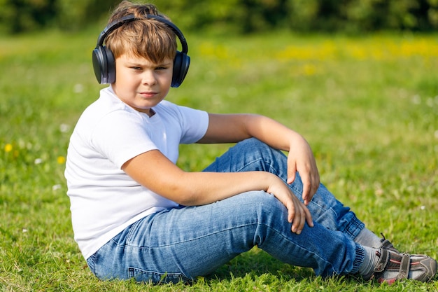 Junge mit Kopfhörern, der Musik hört, während er auf dem Gras im Park sitzt