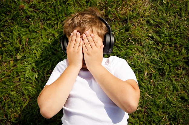 Junge mit Kopfhörern, die Musik hören, die auf dem Gras im Park liegt