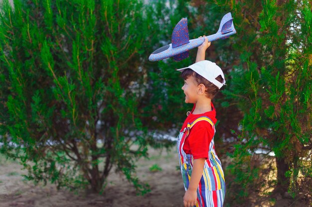 Junge mit Segelflugzeug in den Händen spielt ein Kind mit einem Flugzeug auf der Straße im Park, das draußen spielt...