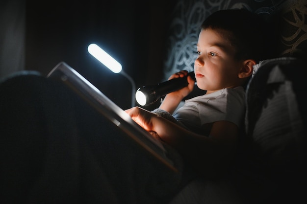 Junge mit Taschenlampe Lesebuch unter Decke zu Hause