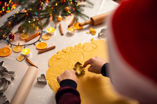 Junge mit Weihnachtsmütze kocht Kekse