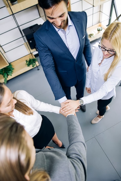 Junge Mitarbeiter, die Hände als Symbol der Einheit im Büro zusammenfügen