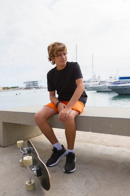 Junge Model Skater sitzt auf einer Bank am Hafen