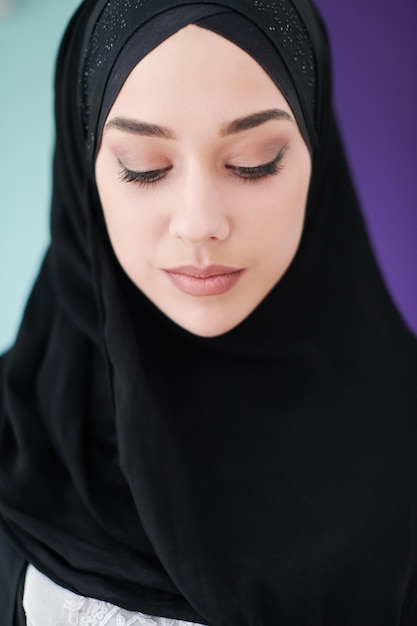 Junge moderne muslimische Geschäftsfrau mit Smartphone in traditioneller Hijab-Kleidung zu Hause