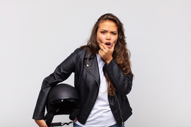 Junge Motorradfahrerin mit offenem Mund und weit geöffneten Augen und Hand am Kinn, die sich unangenehm geschockt fühlt und sagt, was oder wow