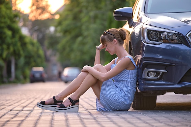 Junge müde Frau, die neben dem Auto sitzt und auf jemanden wartet. Reise- und Urlaubskonzept.