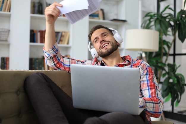 Junge müde Freiberuflerin in Freizeitkleidung, die auf dem Sofa vor dem Laptop sitzt.