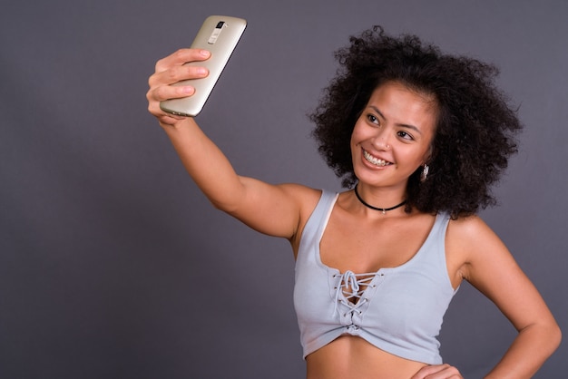 junge multiethnische Afroamerikanerin mit Afro-Haaren gegen graue Wand