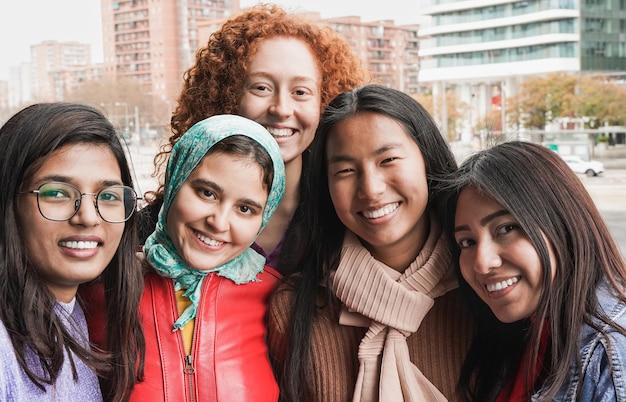 Junge multiethnische Frauen, die im Freien vor der Kamera lächeln Diverse Freundinnen, die gemeinsam Spaß in der Stadt haben