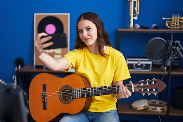 Junge Musikerin macht Selfie per Smartphone mit klassischer Gitarre im Musikstudio