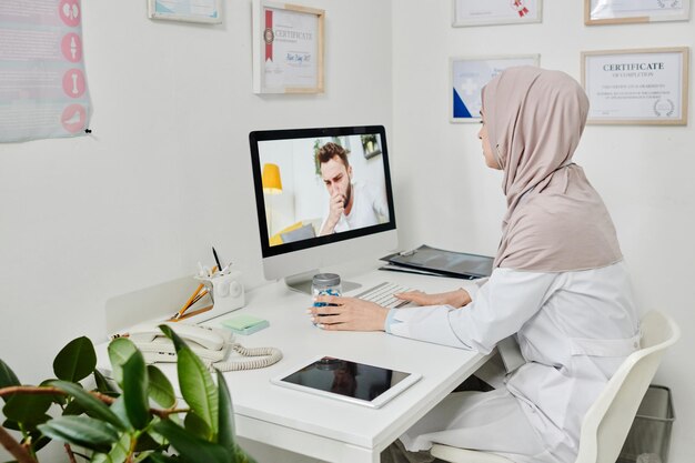 Junge muslimische ärztin im hijab berät online männlichen patienten mit covid