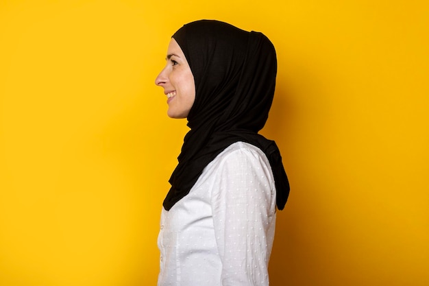 Junge muslimische Frau im Hijab schaut zur Seite und lächelt auf gelbem Hintergrund Banner Profilaufnahme Seitenansicht