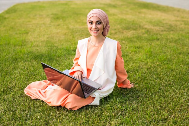 Junge muslimische Frau mit Laptop im Park.